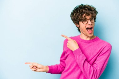 Mavi arka planda izole edilmiş genç beyaz adam işaret parmağıyla fotokopi alanını işaret ederek heyecan ve arzusunu ifade ediyor..