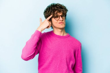 Mavi arka planda izole edilmiş genç beyaz bir adam şakağı parmağıyla işaret ediyor, düşünüyor ve bir göreve odaklanıyor..