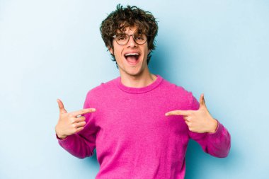 Kafkasyalı genç adam mavi arka planda izole edildi. Parmakları aşağıda, olumlu bir his var..