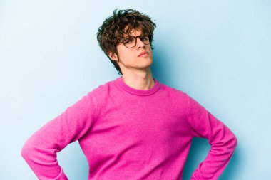 Kafkasyalı genç adam mavi arka planda izole edilmiş hoşnutsuzca kaşlarını çatmış, kollarını kavuşturmuş..