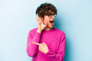 Mavi arka planda izole edilmiş genç beyaz adam bir dedikoduyu dinlemeye çalışıyor..