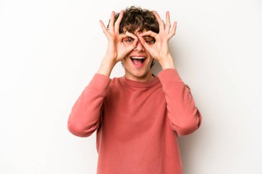 Beyaz arka planda izole genç beyaz adam heyecanlı tamam göz jesti tutmak.