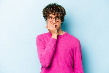 Mavi arka planda izole edilmiş, tırnak yiyen, gergin ve endişeli genç bir beyaz adam..