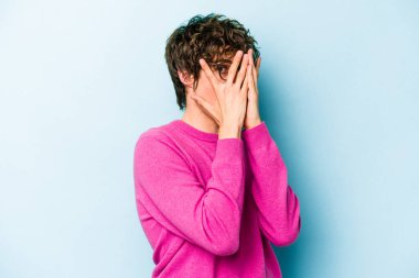 Kafkasyalı genç adam mavi arka planda izole edilmiş. Korkmuş ve gergin parmaklarıyla göz kırp..