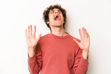 Beyaz arka planda izole edilmiş genç beyaz adam gökyüzüne haykırıyor, yukarı bakıyor, hayal kırıklığına uğramış..