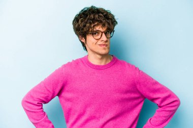 Kafkasyalı genç adam mavi arka planda izole, kafası karışmış, şüpheli ve güvensiz hissediyor..