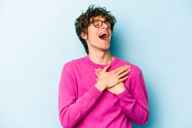 Mavi arka planda izole edilmiş beyaz bir genç, dost bir ifadeye sahip, avuçlarını göğsüne bastırıyor. Aşk konsepti.