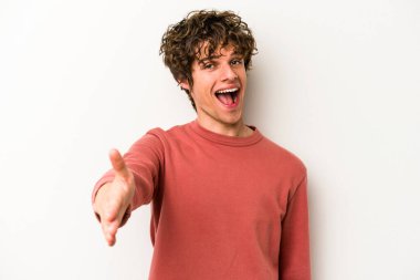 Beyaz arka planda izole edilmiş genç beyaz bir adam selamlama jesti olarak kameraya elini uzatıyor..