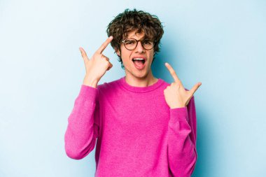 Mavi arka planda izole edilmiş genç beyaz adam işaret parmağıyla bir hayal kırıklığı jesti gösteriyor..