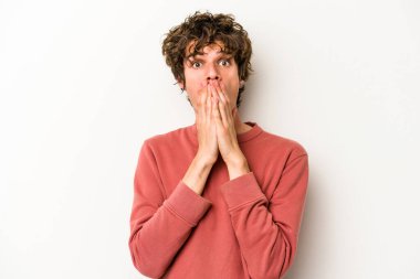 Beyaz arka planda izole edilmiş genç beyaz adam elleriyle ağzını kapatırken şok oldu..
