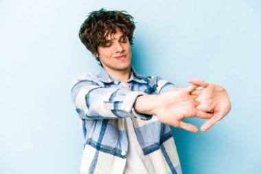 Mavi arka planda izole edilmiş genç beyaz adam kollarını uzatıyor, rahat bir konumda..