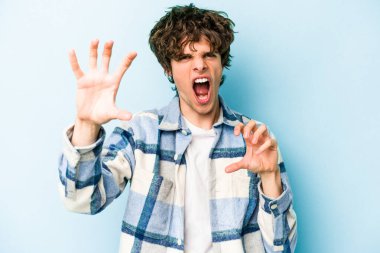 Mavi arka planda izole edilmiş genç beyaz adam gergin elleriyle çığlık atıyor..