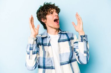 Kafkasyalı genç adam mavi arka planda izole edilmiş gökyüzüne haykırıyor, yukarı bakıyor, hayal kırıklığına uğramış..