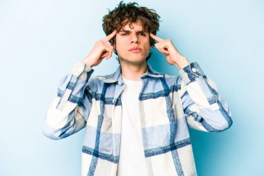 Kafkasyalı genç adam mavi arka planda izole edilmiş bir göreve odaklanmış, parmaklarını işaret ediyor..