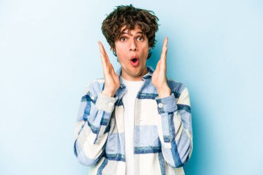 Kafkasyalı genç adam mavi arka planda izole edildi. Şaşırdı ve şok oldu..