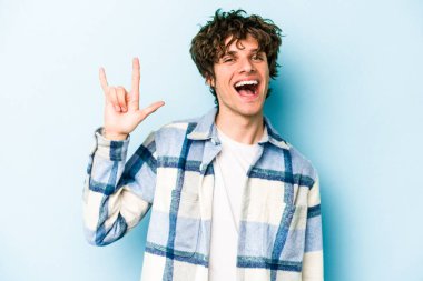 Mavi arka planda izole edilmiş genç beyaz adam boynuzlarını devrim konsepti olarak gösteriyor..