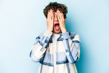 Mavi arka planda izole edilmiş genç beyaz adam yüzünün yarısını palmiye ile kaplayarak eğleniyor..