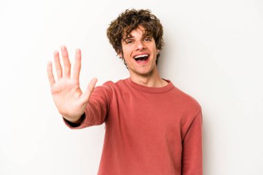 Beyaz arka planda izole edilmiş genç beyaz bir adam gülümseyerek beş numarayı parmaklarıyla gösteriyor..