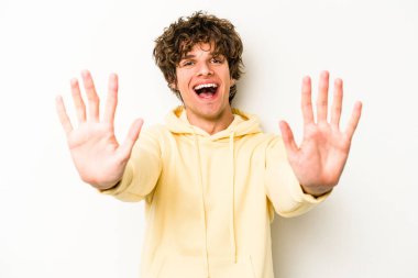 Beyaz arka planda izole edilmiş beyaz tenli genç adam on numarayı elleriyle gösteriyor..