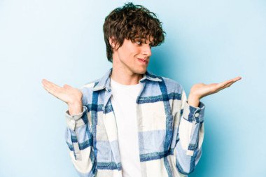 Kafkasyalı genç adam mavi arka planda izole edilmiş. Kafası karışmış ve omuz silkiyor. Kopya alanını tutmak için..