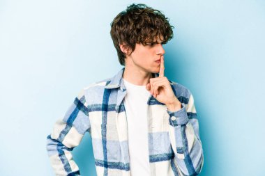 Mavi arka planda izole edilmiş genç beyaz bir adam ya sır saklıyor ya da sessizlik istiyor..