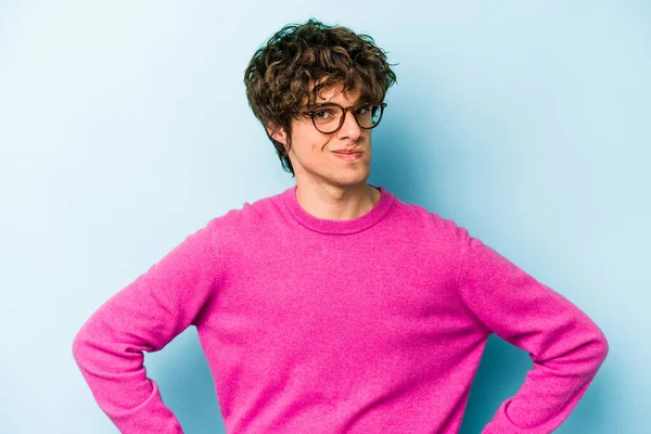 Kafkasyalı genç adam mavi arka planda izole, kafası karışmış, şüpheli ve güvensiz hissediyor..