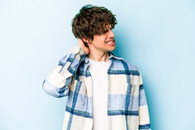 Kafkasyalı genç adam mavi arka planda izole edilmiş. Yorgun ve uykulu. Elini başının üstünde tutuyor..