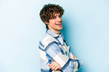 Mavi arka planda kendini güvende hisseden, kararlılıkla kollarını kavuşturan genç beyaz bir adam..