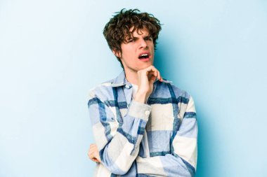 Kafkasyalı genç adam mavi arka planda izole edilmiş şüpheli, belirsiz, seni muayene ediyor..