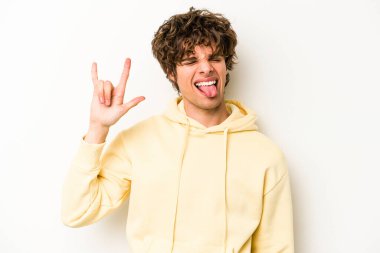 Beyaz arka planda izole edilmiş genç beyaz bir adam parmaklarıyla kaya hareketi gösteriyor.