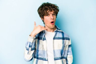 Mavi arka planda izole edilmiş genç beyaz bir adam bir şeye gülüyor, ağızlarını ellerle kapatıyor..