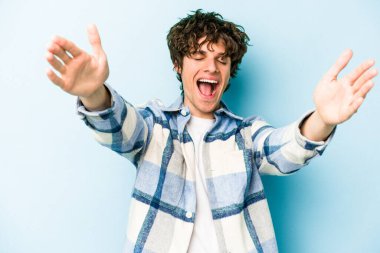 Mavi arka planda izole edilmiş genç beyaz adam kameraya sarıldığı için kendinden emin hissediyor..