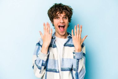 Mavi arka planda izole edilmiş genç beyaz adam on numarayı elleriyle gösteriyor..