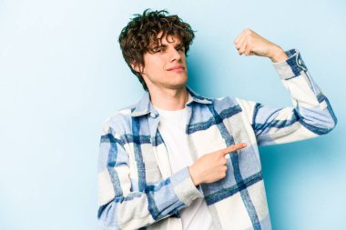 Mavi arka planda izole edilmiş genç beyaz adam güçlü bir hareket sergiliyor kollarıyla, kadınsı gücün sembolü.