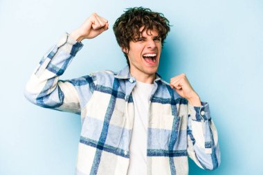 Kafkasyalı genç adam mavi arka planda izole edilmiş kaygısız ve heyecanlı tezahüratlar yapıyor. Zafer konsepti.