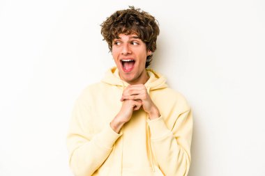 Beyaz arka planda izole edilmiş genç beyaz bir adam şans için dua ediyor, şaşırmış ve ağzını açıp önüne bakıyor..