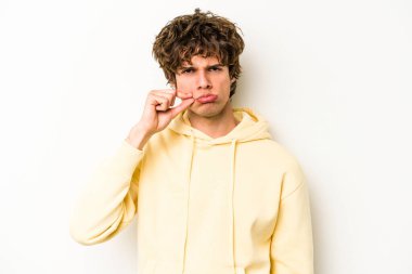 Beyaz arka planda izole edilmiş beyaz tenli genç bir adam parmakları dudaklarında bir sır saklıyor..