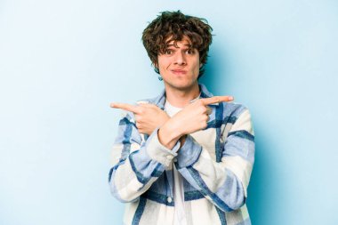 Mavi arka plan noktalarında izole genç beyaz adam, iki seçenek arasında seçim yapmaya çalışıyor.