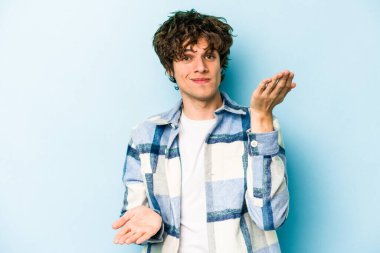 Mavi arka planda izole genç beyaz adam kollarıyla ölçek yapar, mutlu ve kendinden emin hisseder..