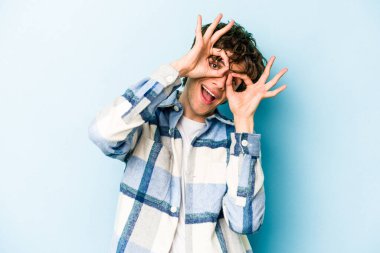 Mavi arka planda izole edilmiş genç beyaz adam gözlerinde sorun olmadığını gösteriyor.