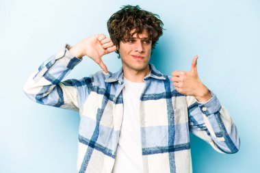 Kafkasyalı genç adam mavi arka planda izole edilmiş, baş parmağını kaldırıyor, zor seçim konsepti.