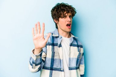 Mavi arka planda izole genç beyaz adam yakın bir tehlike nedeniyle şoka uğruyor