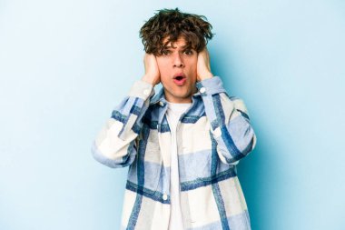 Kafkasyalı genç adam mavi arka planda izole edilmiş kulakları kulaklarıyla kapatıyor çok fazla ses duymamaya çalışıyor..