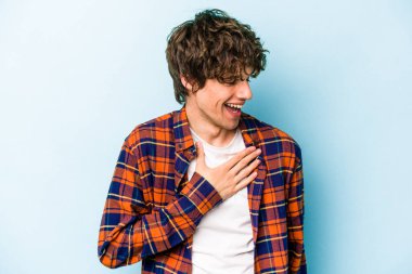 Kafkasyalı genç adam mavi arka planda izole olmuş gülüyor, elini yüreğine koyuyor, mutluluk kavramını koruyor..