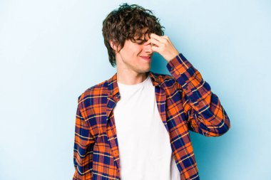 Kafkasyalı genç bir adam mavi arka planda izole edilmiş, başı ağrıyor, yüzüne dokunuyor..