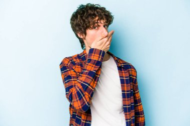 Kafkasyalı genç adam mavi arka planda izole edilmiş ağzı kapalı ve elleri endişeli görünüyor..