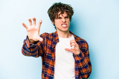 Mavi arka planda izole edilmiş genç beyaz adam pençelerini kedi taklidi yaparken gösteriyor, agresif bir hareket..