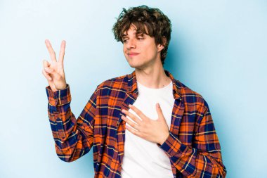 Kafkasyalı genç adam mavi arka planda izole edilmiş yemin ediyor, elini göğsüne koyuyor..