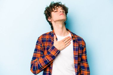 Kafkasyalı genç adam mavi arka planda izole edilmiş yemin ediyor, elini göğsüne koyuyor..