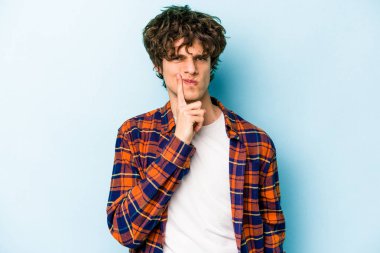 Kafkasyalı genç adam mavi arka planda izole edilmiş düşünüyor ve bakıyor, yansıtıyor, düşünüyor, bir fantezi kuruyor..